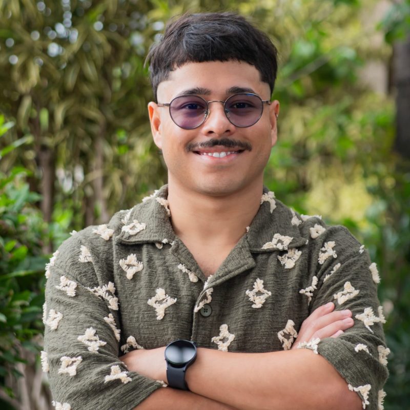 Foto do psicólogo Alexandre José da Costa Santos, especialista em Psicanálise na clínica Presente Psicologia. Ele usa óculos, tem barba, veste uma camisa preta e olha de forma atenta e acolhedora para a câmera.
