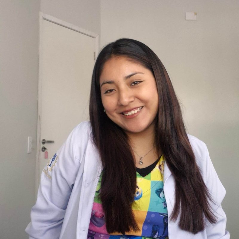 Foto da psicóloga Mikaela Adriana Ticona Mamani, especialista em Terapia Cognitivo-Comportamental (TCC) e Ciência ABA na clínica Presente Psicologia. Ela tem cabelos escuros, sorri de forma acolhedora e veste um blazer verde.