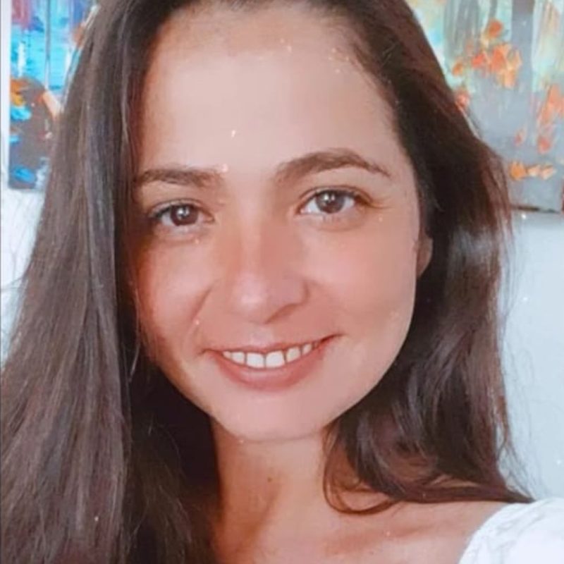 Foto da psicóloga Adriana Roberta Ribeiro, especialista em Psicologia Analítica na clínica Presente Psicologia. Ela tem longos cabelos escuros, sorri suavemente de forma acolhedora e veste uma blusa branca.