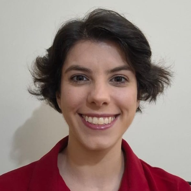 Foto da psicóloga Bruna Brito Finardi, especialista em Gestalt-terapia na clínica Presente Psicologia, sorrindo e vestindo camisa vermelha.