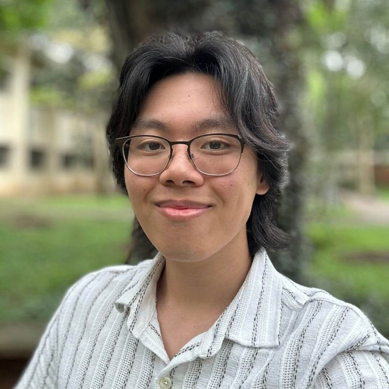 Foto do psicólogo Felipe Yuichi Morinishi, especialista em Terapia de Aceitação e Compromisso (ACT) e Neuropsicologia na clínica Presente Psicologia. Ele tem cabelos escuros, usa óculos de grau, sorri de forma amigável e veste uma camisa clara listrada, com um fundo verde de árvores desfocado.