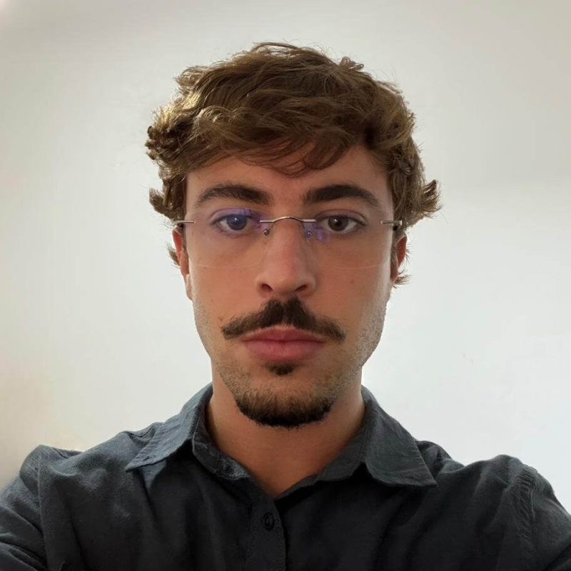 Foto do psicólogo Rafael Souza Alves, especialista em Psicanálise na clínica Presente Psicologia. Ele tem cabelos curtos, usa óculos de grau, possui barba e bigode, e veste uma camisa escura, transmitindo uma postura analítica e atenta.