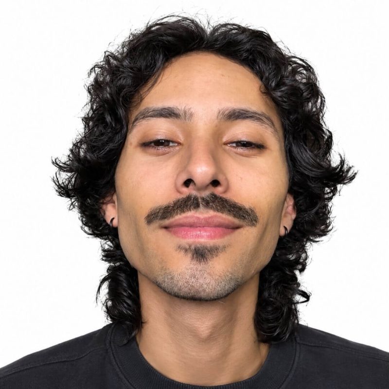 Foto do psicólogo Vitor Sousa Silva, especialista em Psicologia Analítica na clínica Presente Psicologia. Ele tem cabelos escuros ondulados, bigode e cavanhaque, veste uma blusa preta e transmite uma postura expressiva e acolhedora.